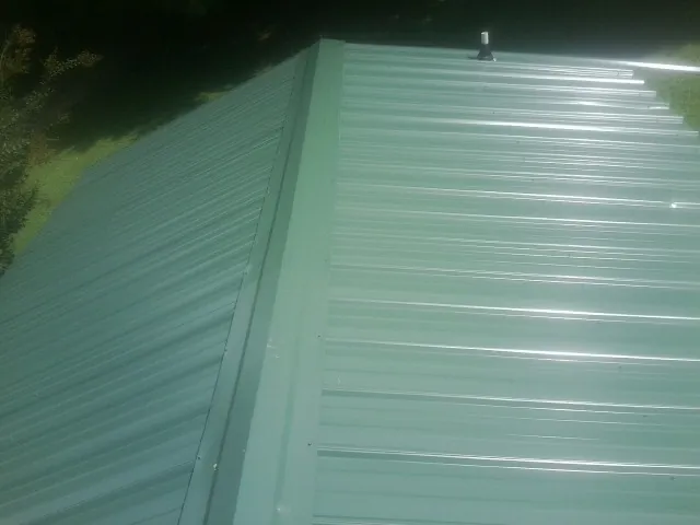 New green metal panels meeting at the ridge of a roof — Flat Roof Repair work by our crew in Redfield