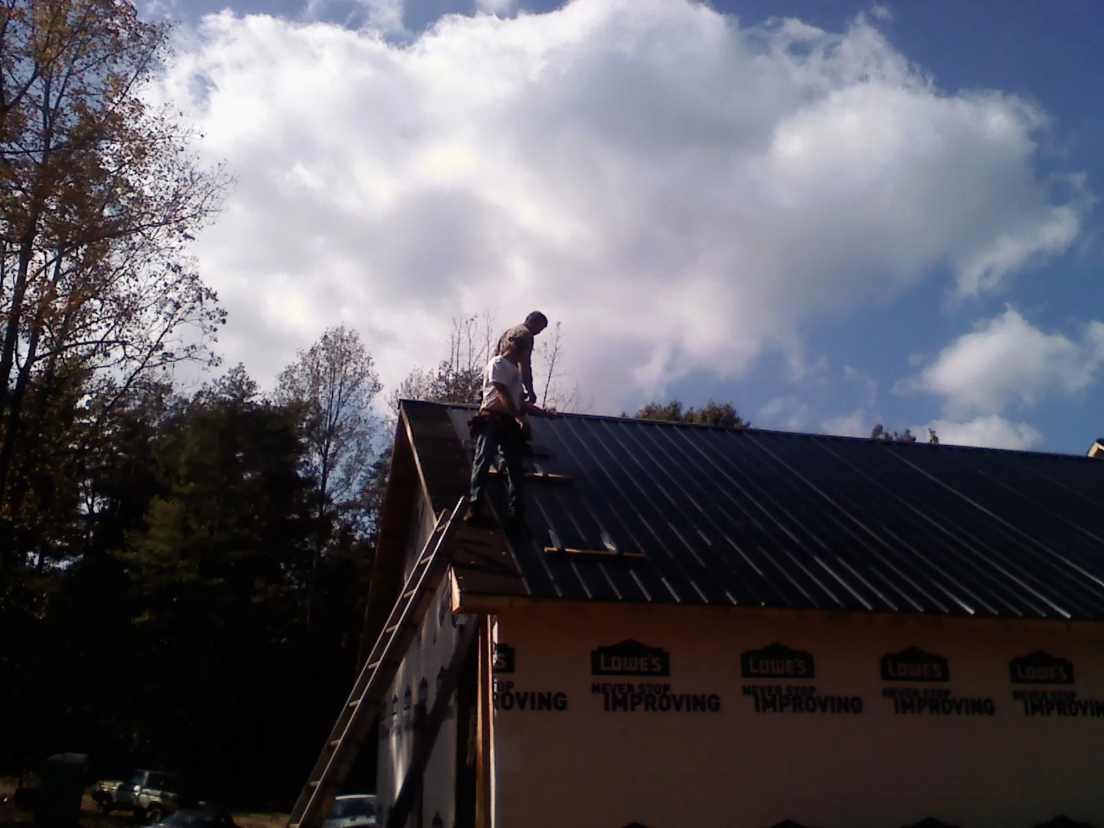 Roofer fastening dark metal panels high against a cloudy sky, from a Roof Inspection job in Redfield
